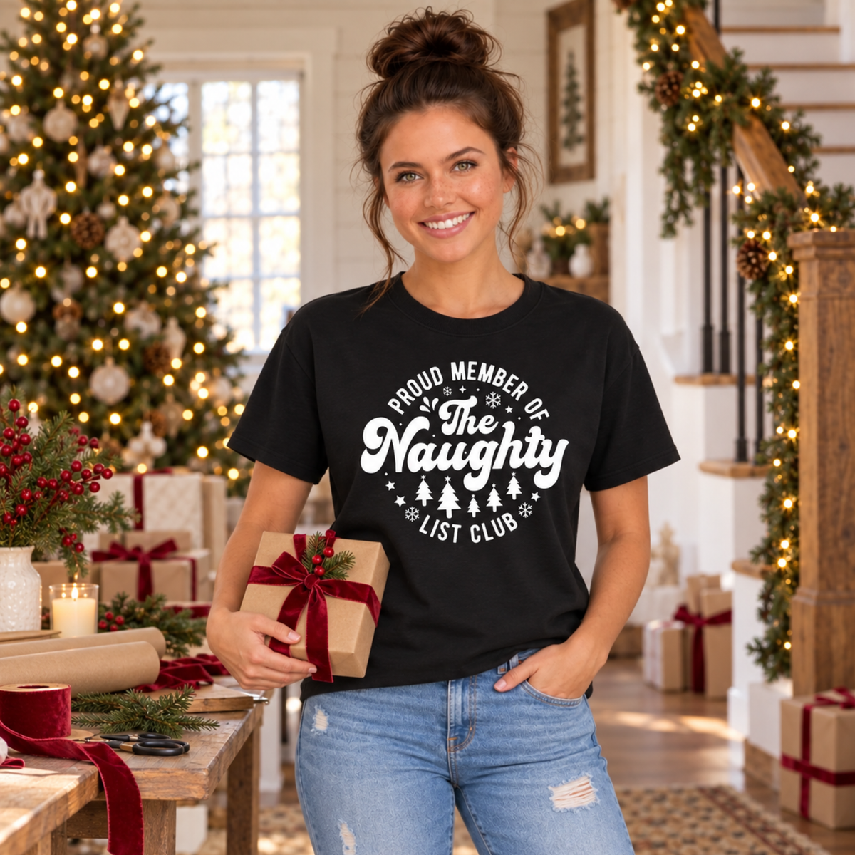 Woman wearing a black T-shirt with a white Proud Member of the Naughty List Club design while holding a wrapped Christmas gift.