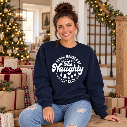 Woman wearing a navy crewneck sweatshirt with a white Proud Member of the Naughty List Club design while seated among Christmas gifts.
