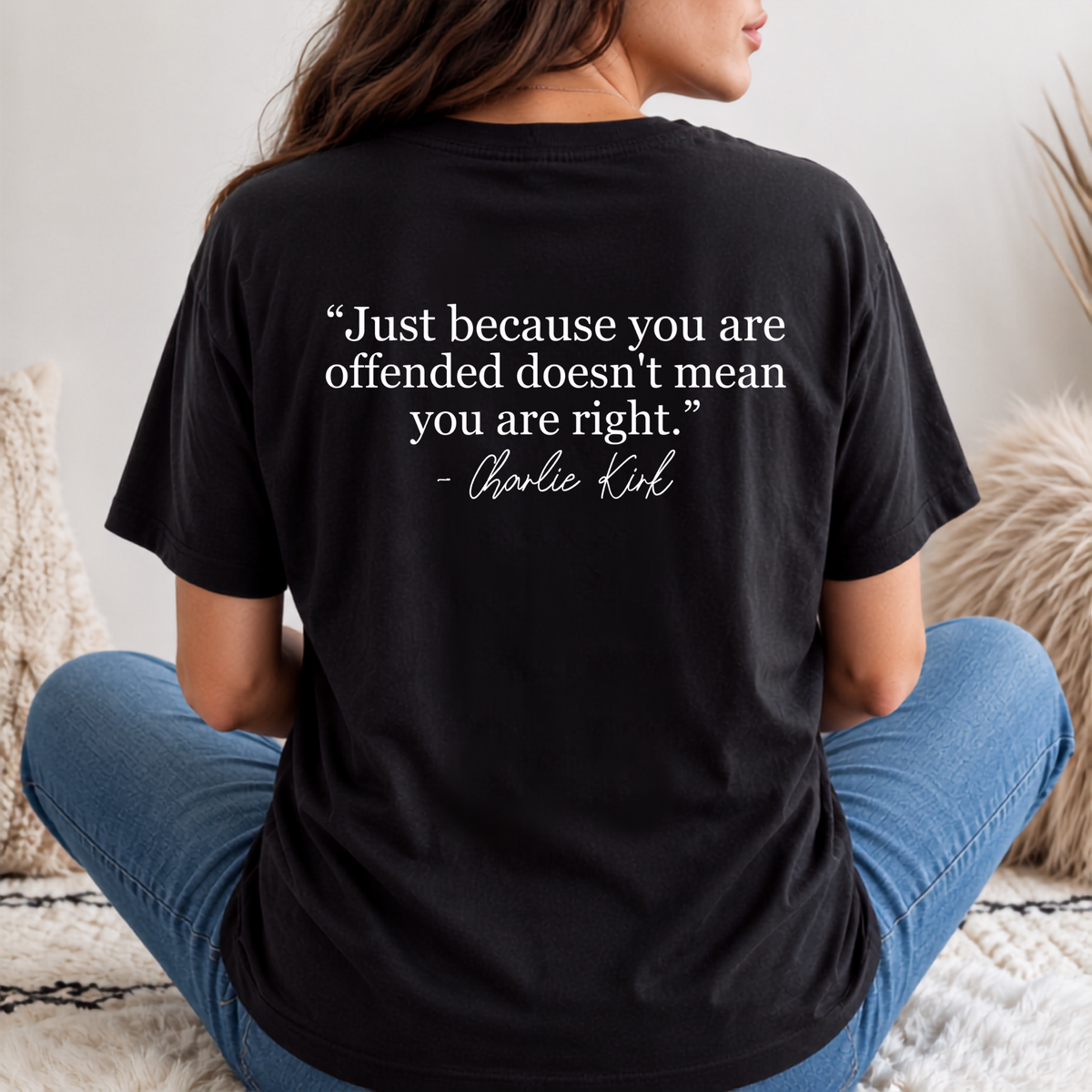Back view of a woman in a black T-shirt with a white quote graphic, seated on outdoor steps.
