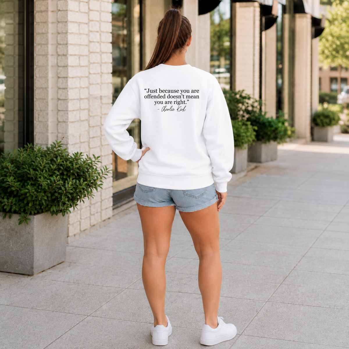 Back view of a woman wearing a white crewneck sweatshirt with a black quote graphic.