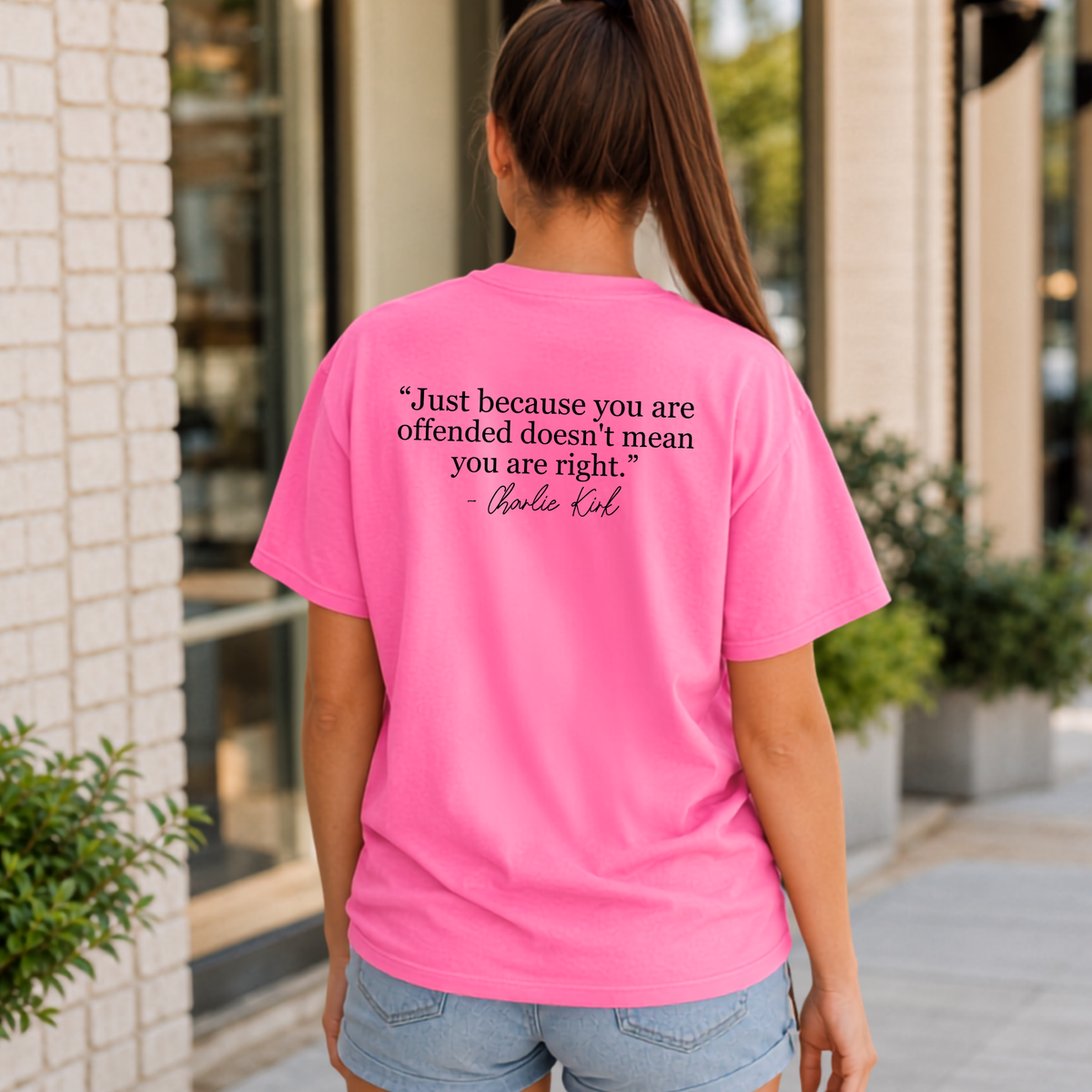 Back view of a woman wearing a bright pink T-shirt with a black quote graphic.
