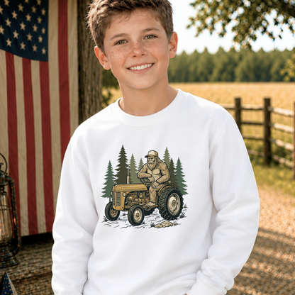 Youth model wearing a white crewneck sweatshirt with a woodland tractor graphic.