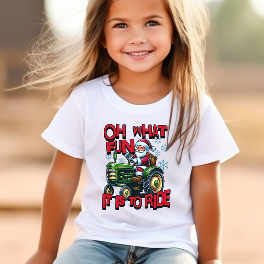 Young girl in a white holiday T-shirt featuring Santa Claus driving a green tractor with bold red Christmas lettering