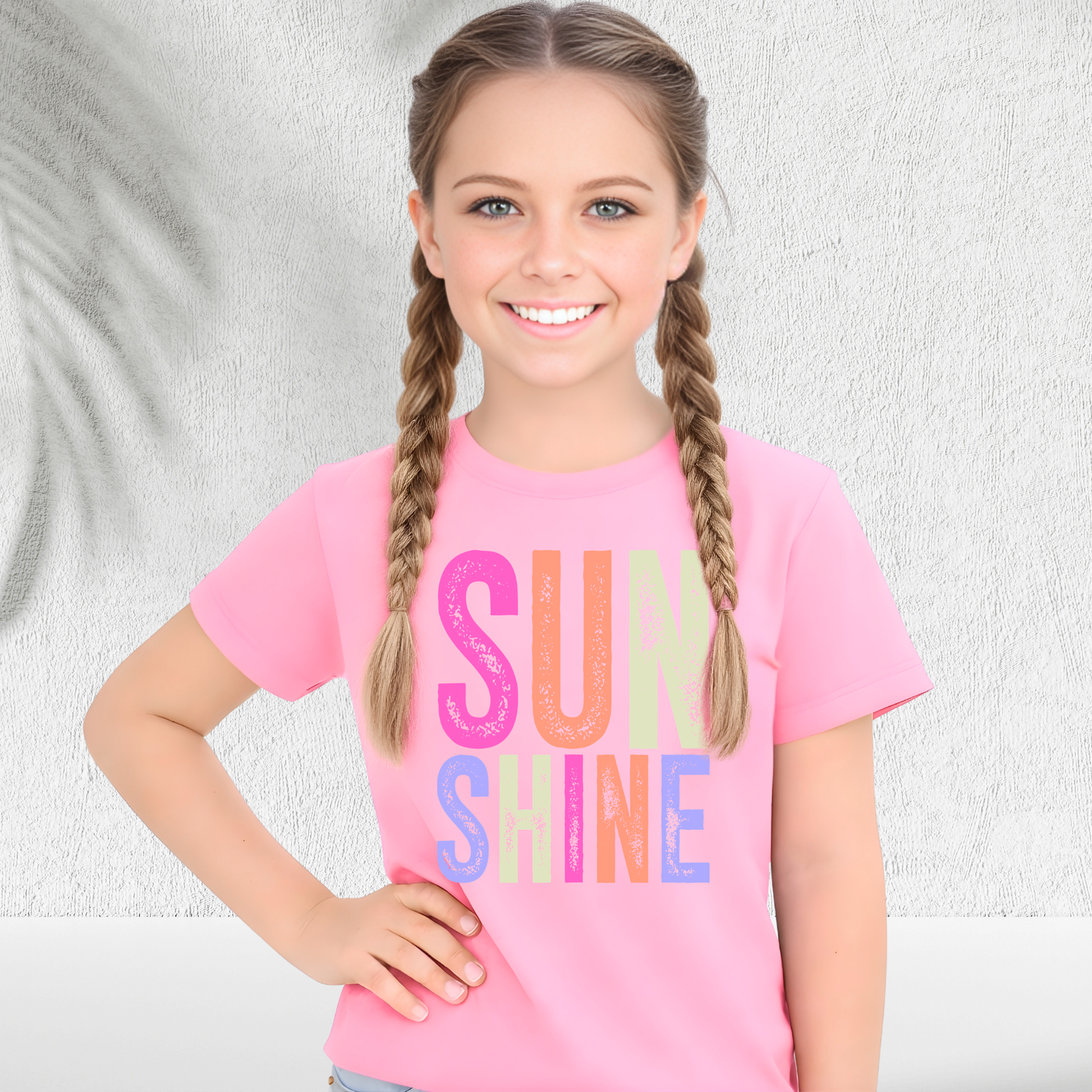 Young girl wearing a pink t-shirt with 'SUN SHINE' in colorful letters against a light background