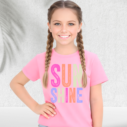 Young girl wearing a pink t-shirt with 'SUN SHINE' in colorful letters against a light background