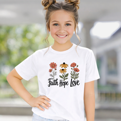 Young girl wearing a white t-shirt with floral designs and 'Faith Hope Love' text.