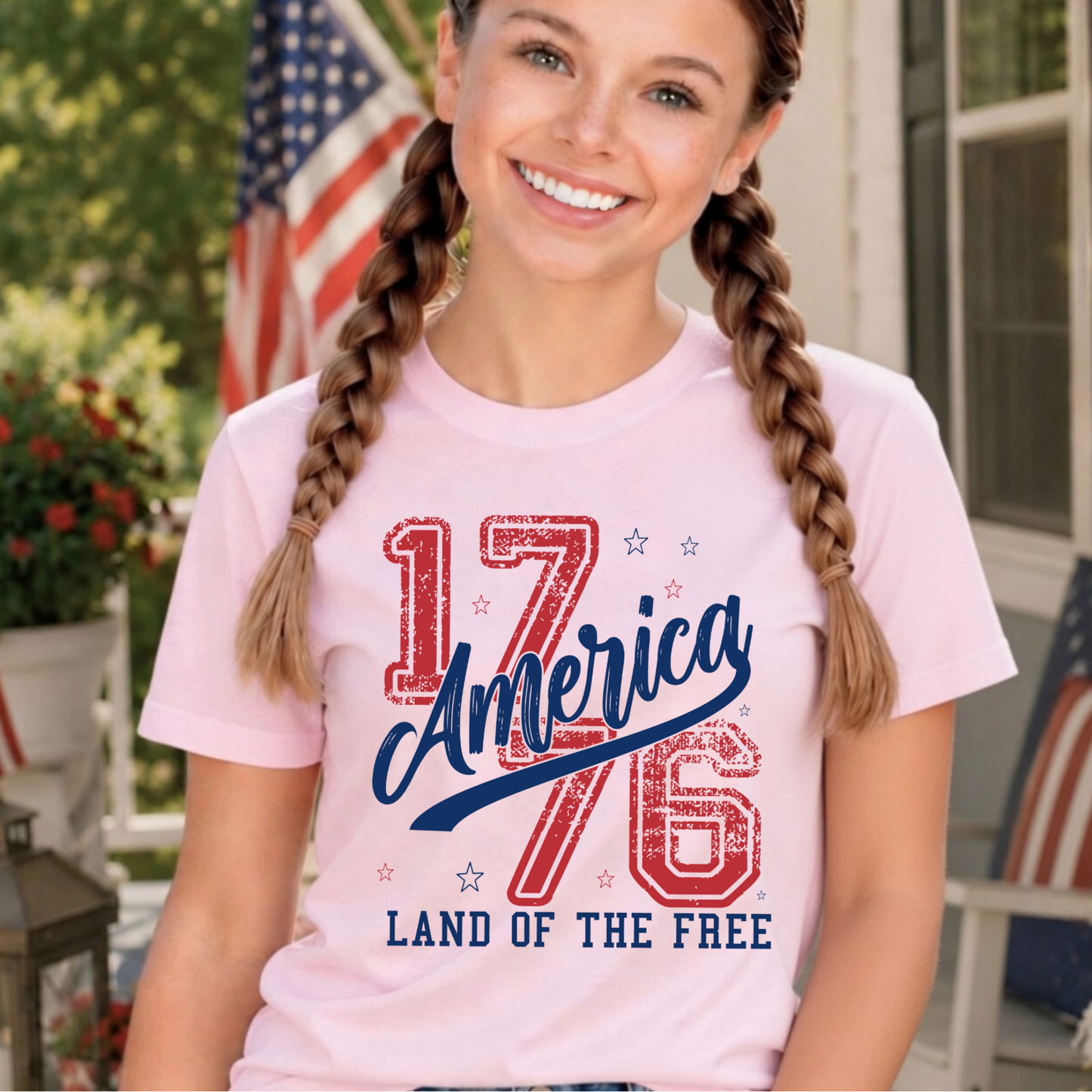 Young girl wearing a pink t-shirt with '1776 America Land of the Free' design, standing outdoors.