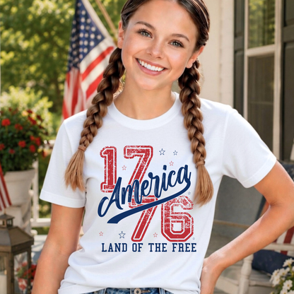youth girl wearing a white t-shirt with '1776 America Land of the Free' design, standing outdoors.