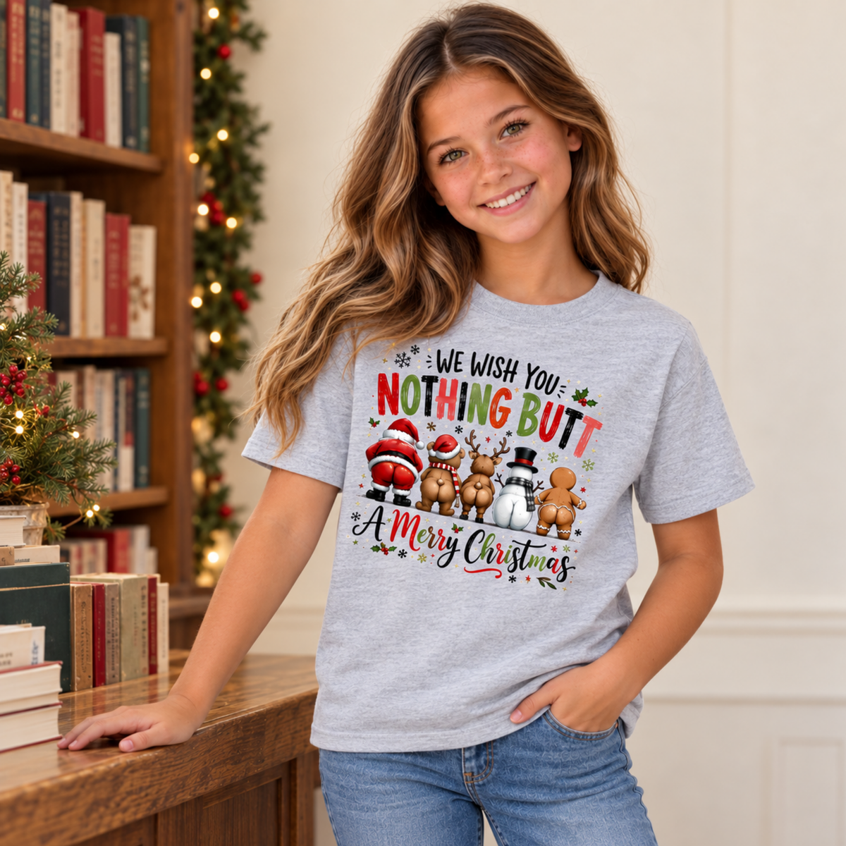 Youth model wearing a sports gray T-shirt with We Wish You Nothing Butt a Merry Christmas design with festive characters shown from behind in a decorated Christmas bookstore