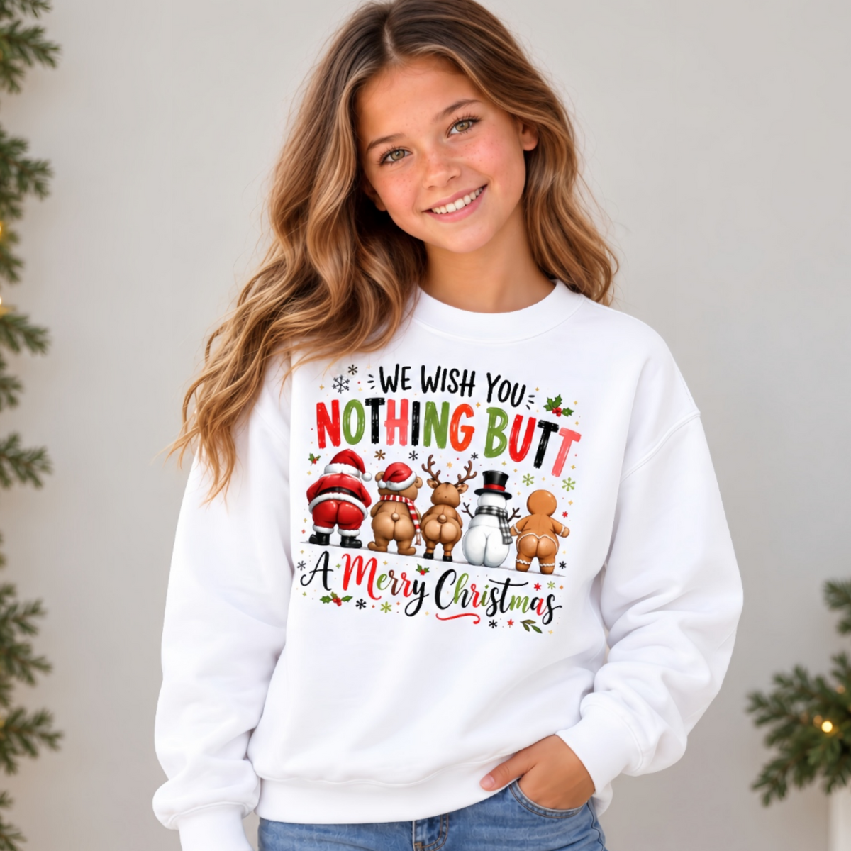 Youth model wearing a white crewneck sweatshirt with We Wish You Nothing Butt a Merry Christmas design with festive characters shown from behind against a simple holiday backdrop