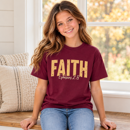 Young model seated by a farmhouse window wearing a maroon youth T-shirt with distressed gold FAITH lettering and white Ephesians 2:8 script.