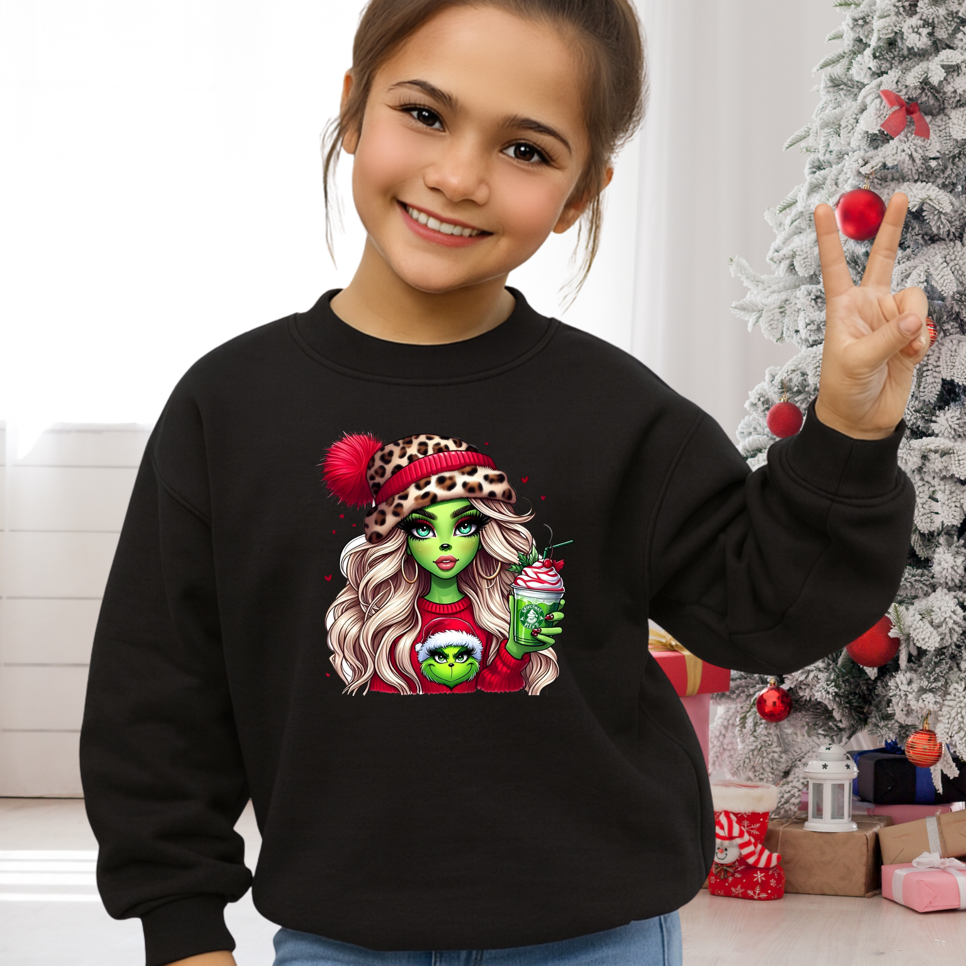 Child wearing a black sweatshirt with a festive design, standing in front of a decorated Christmas tree.