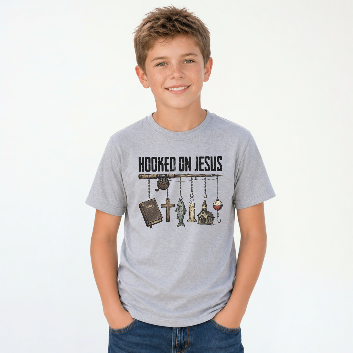 Smiling boy wearing a sports gray youth T-shirt with a Hooked On Jesus fishing rod graphic featuring a Bible, cross, fish, church, and bobber.