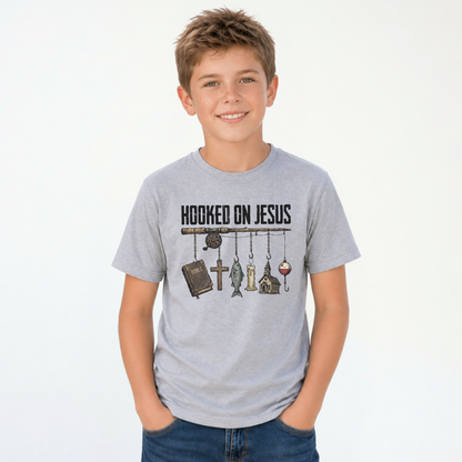 Smiling boy wearing a sports gray youth T-shirt with a Hooked On Jesus fishing rod graphic featuring a Bible, cross, fish, church, and bobber.