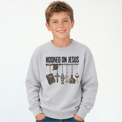 Smiling boy wearing a sports gray youth sweatshirt with a Hooked On Jesus fishing rod graphic featuring a Bible, cross, fish, church, and bobber.