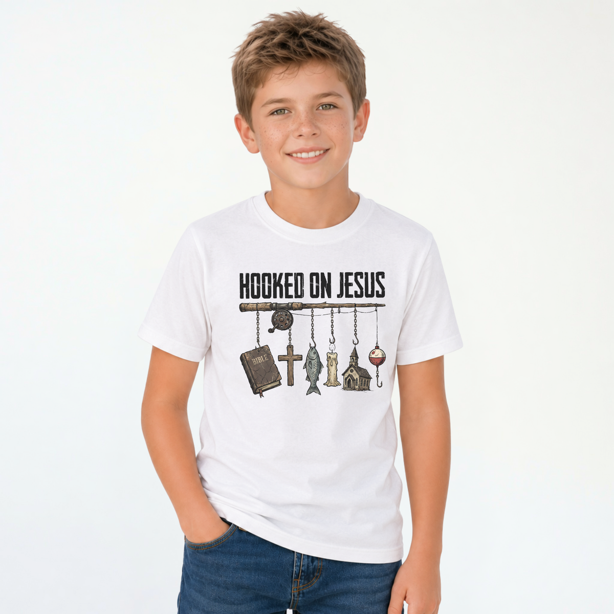 Smiling boy wearing a white youth T-shirt with a Hooked On Jesus fishing rod graphic featuring a Bible, cross, fish, church, and bobber.
