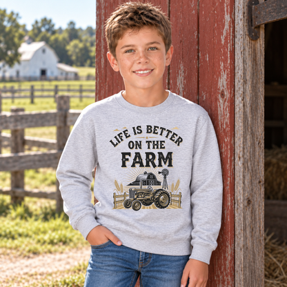 Boy in a sports gray youth Life Is Better on the Farm sweatshirt at a red barn doorway.