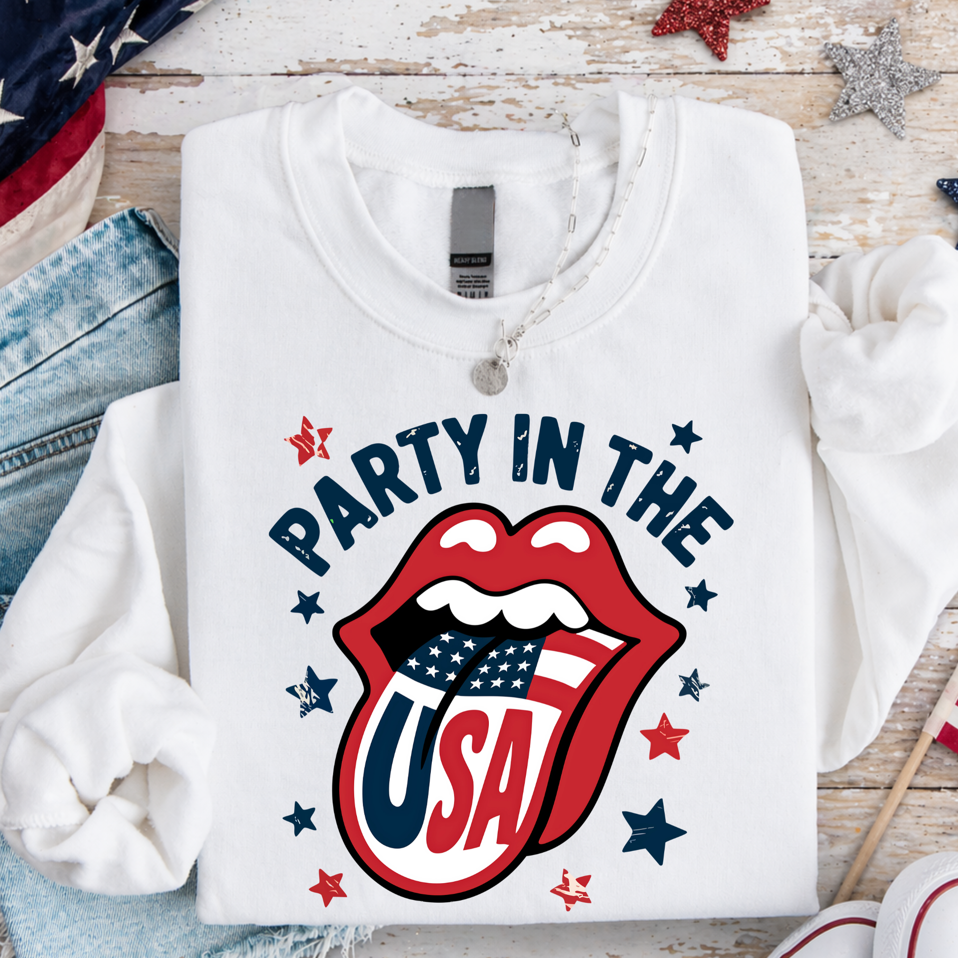 White sweatshirt with 'Party in the USA' graphic on a wooden surface with American flag and stars.