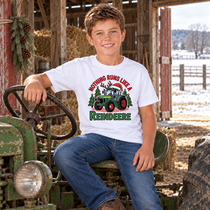 Boy in a white Nothing Runs Like a Reindeere T-shirt seated on a vintage green tractor in a snowy barn.