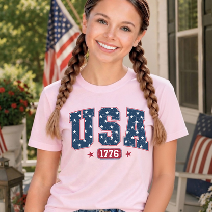 Young girl wearing a pink 'USA 1776' t-shirt with an American flag in the background.