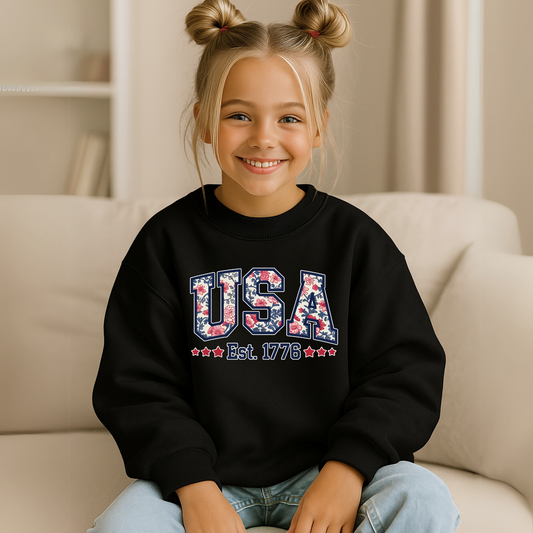 Youth girl wearing black USA Est. 1776 sweatshirt, relaxed pose at home.

