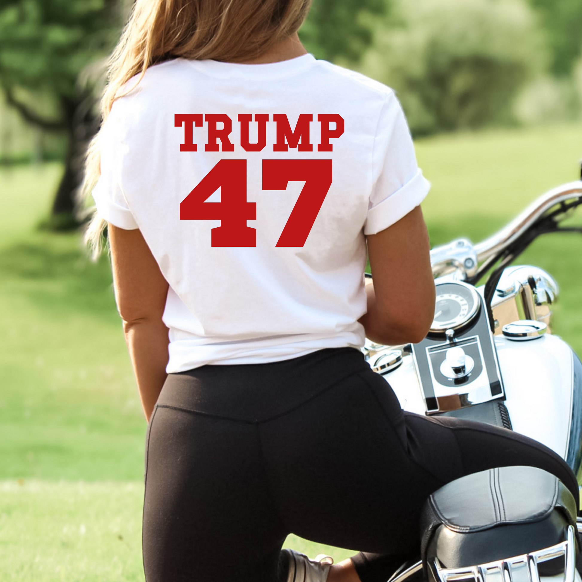 Woman wearing white Trump 47 tee sitting on motorcycle – back view