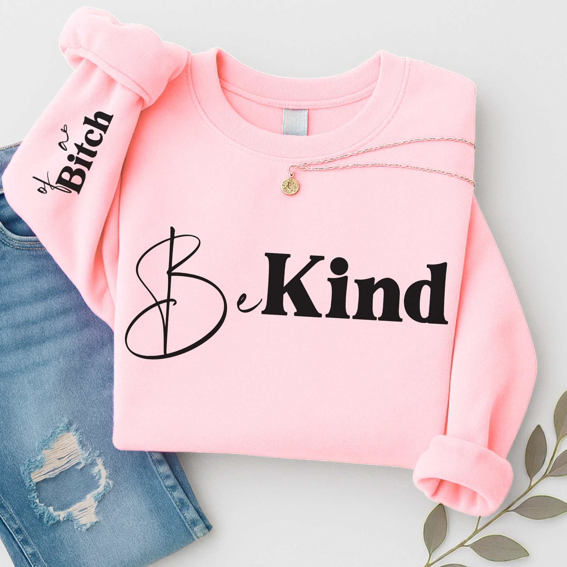 Pink sweatshirt with 'Be Kind' text on a light gray background