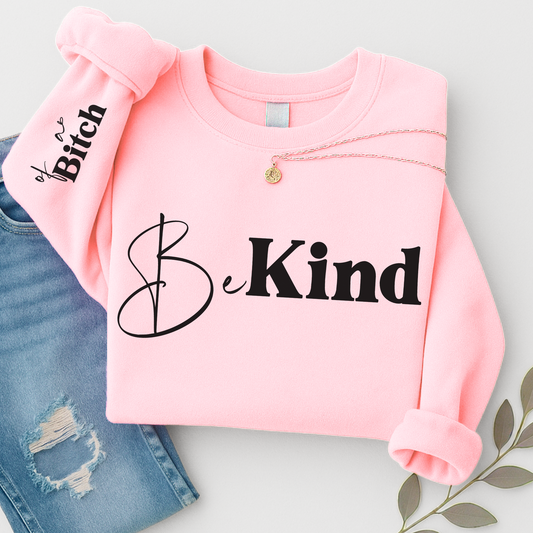 Pink sweatshirt with 'Be Kind' text on a light gray background