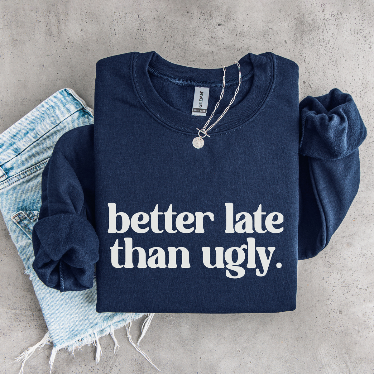 Navy Better Late Than Ugly youth crewneck sweatshirt flat lay with white lettering, styled with denim and a necklace.