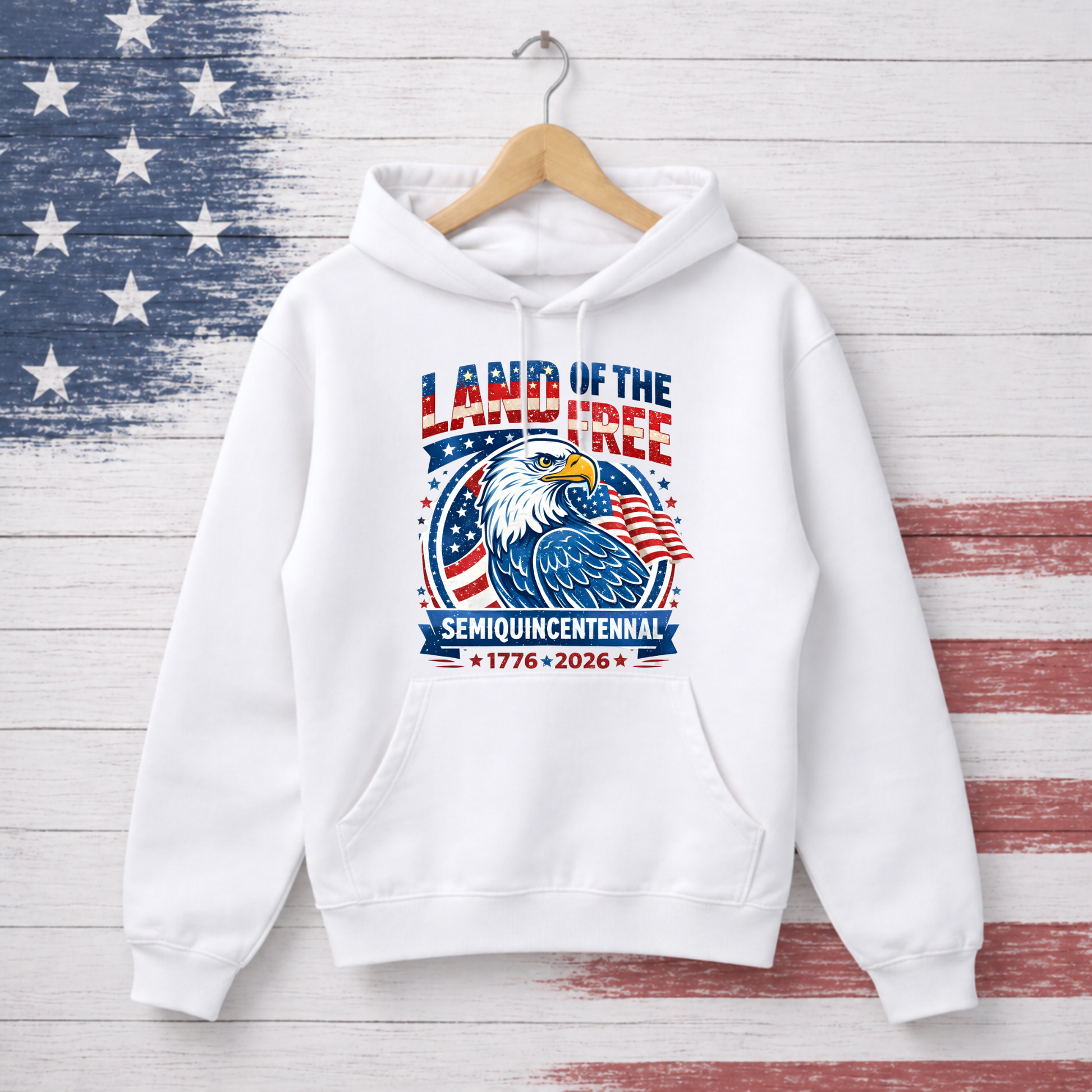 White hoodie with 'Land of the Free' design on a wooden background with American flag pattern