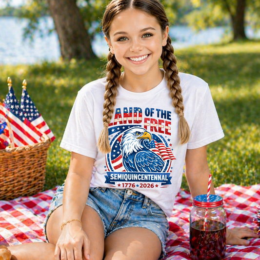 Young girl wearing a t-shirt with a America 250 patriotic design, sitting on a picnic blanket by a lake.