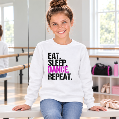 Girl seated on a studio bench in a white youth Eat Sleep Dance Repeat sweatshirt beside ballet shoes.