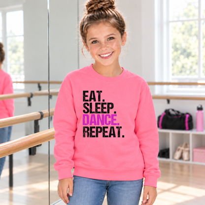 Girl in a bright pink youth Eat Sleep Dance Repeat sweatshirt standing beside a dance studio barre.