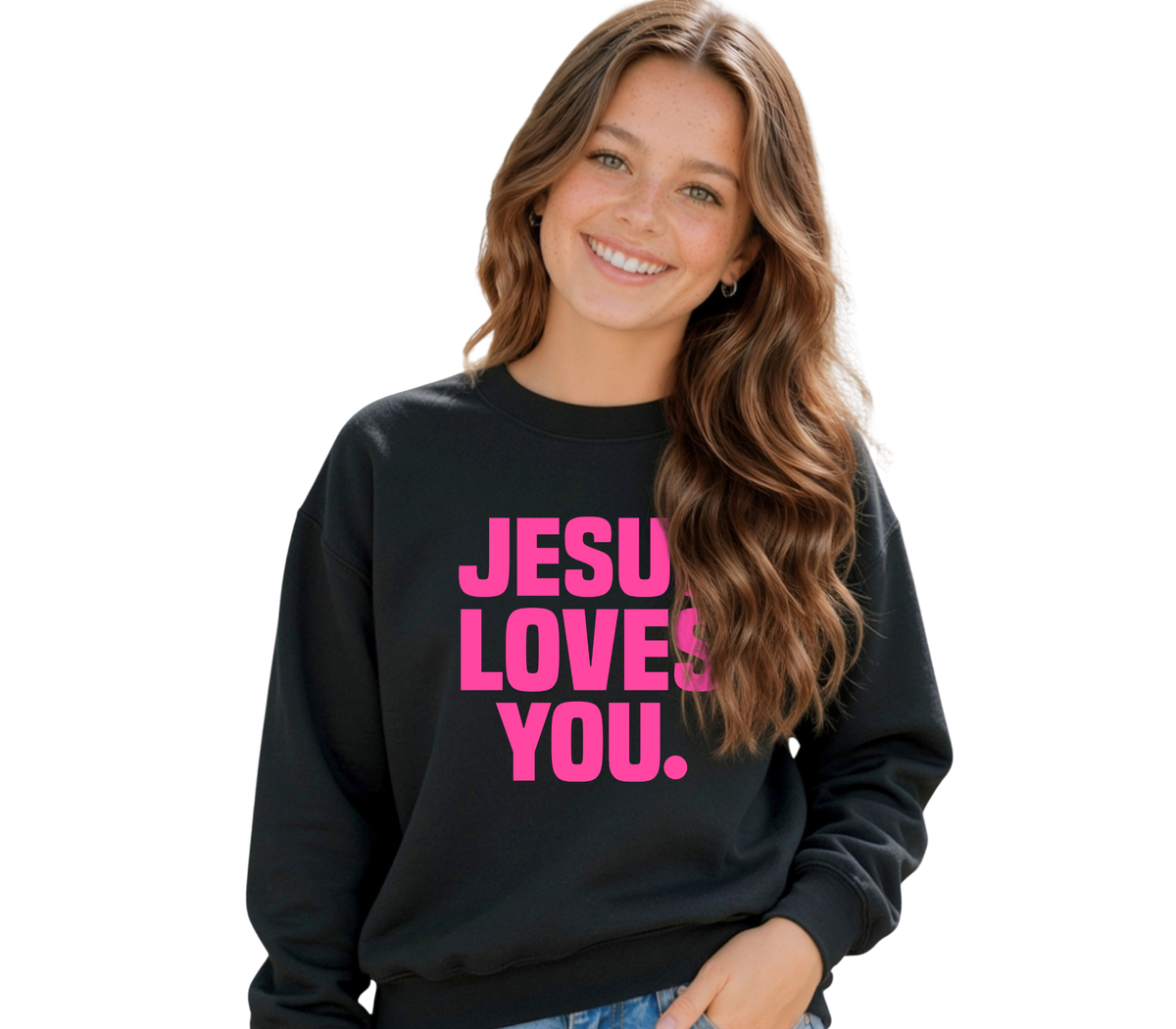 A smiling young woman with long wavy brown hair wears a black crewneck sweatshirt with the phrase 'JESUS LOVES YOU.' printed in bold pink letters across the front, set against a plain white background.