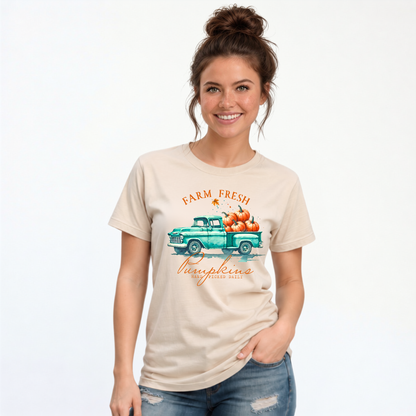 Woman wearing a sand T-shirt with a teal truck full of pumpkins and Farm Fresh Pumpkins design on a white background.