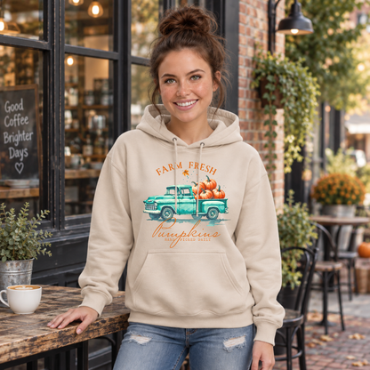 Woman wearing a sand hoodie with a teal pumpkin truck and Farm Fresh Pumpkins design outside a fall cafe.