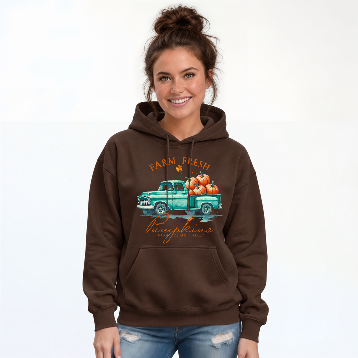 Woman wearing a brown hoodie with a teal truck full of pumpkins and Farm Fresh Pumpkins design on a white background.