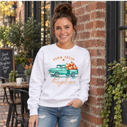 Woman wearing a white sweatshirt with a teal truck full of pumpkins and Farm Fresh Pumpkins design by a brick cafe.