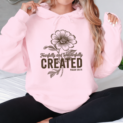 Light pink hoodie with Fearfully and Wonderfully Created floral design worn seated