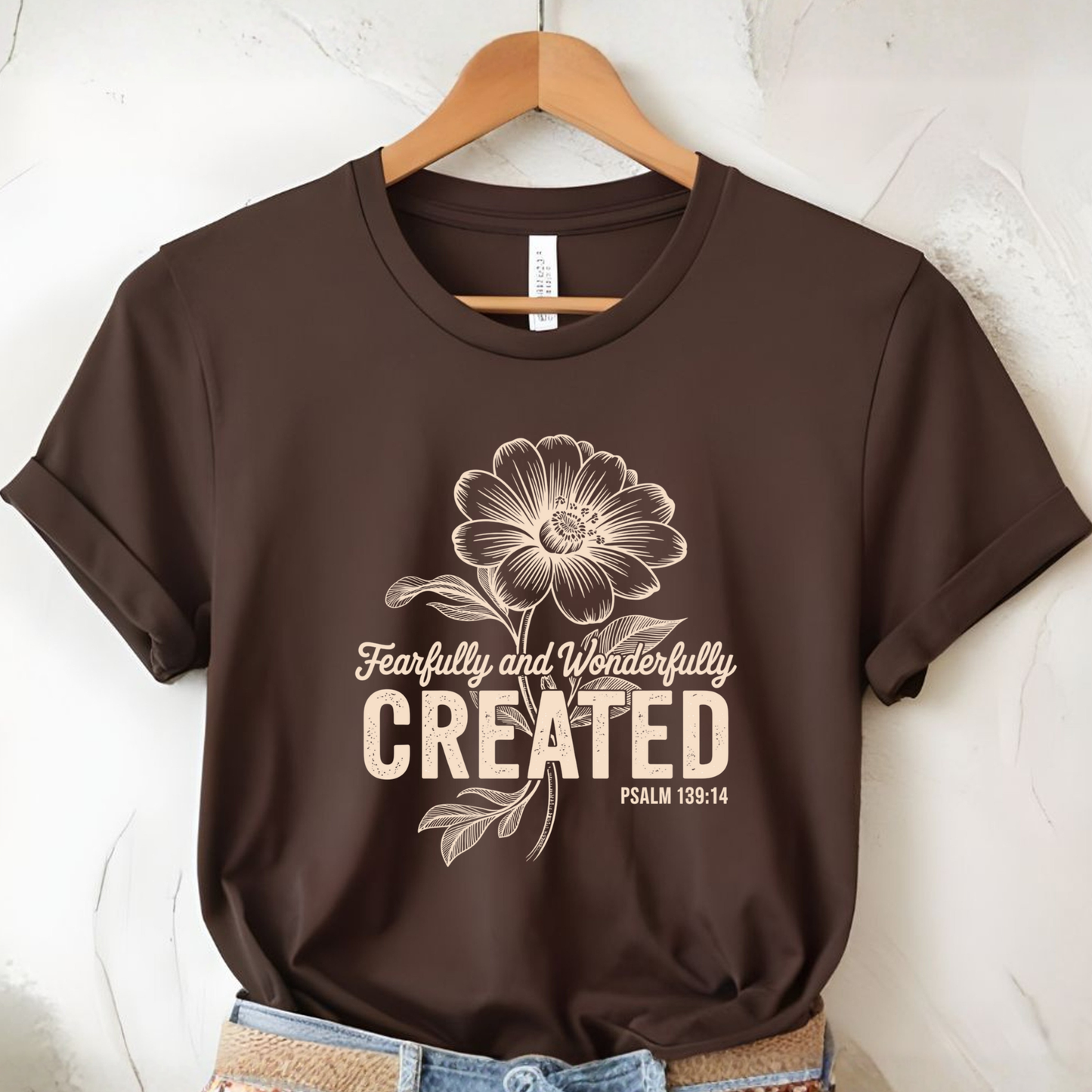 Light pink t-shirt with Fearfully and Wonderfully Created floral design on hanger and jeans