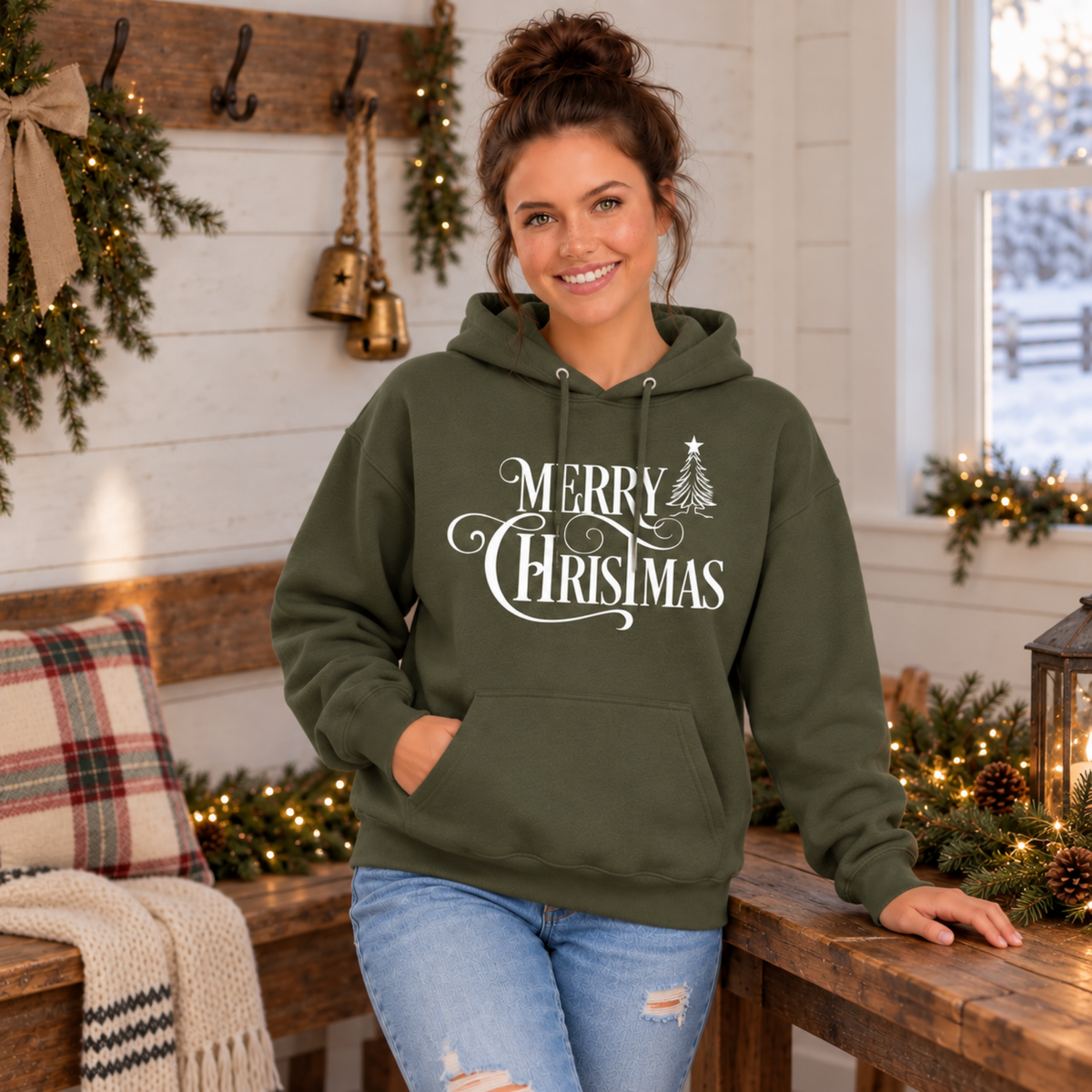 Military green Merry Christmas hoodie with white script and Christmas tree artwork, modeled indoors with Christmas decorations.