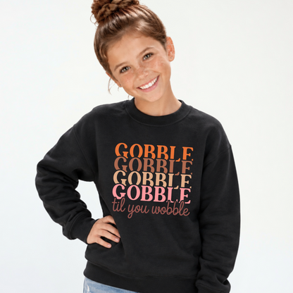 Girl modeling a black youth sweatshirt with the retro Gobble Til You Wobble Thanksgiving design.