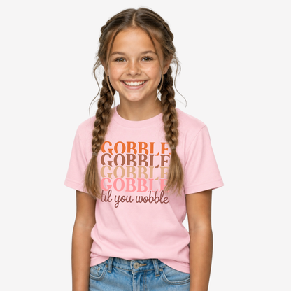 Girl modeling a light pink youth T-shirt with the retro Gobble Til You Wobble Thanksgiving design.