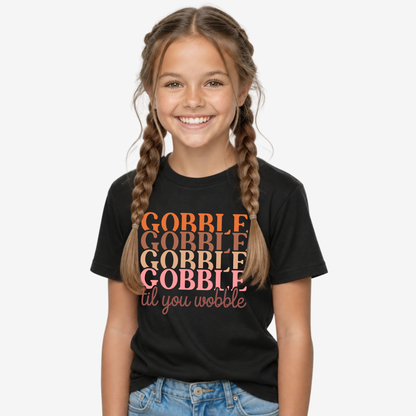 Girl modeling a black youth T-shirt with the retro Gobble Til You Wobble Thanksgiving design.