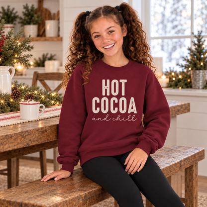 Girl wearing a maroon youth sweatshirt with Hot Cocoa and Chill design in a festive winter kitchen