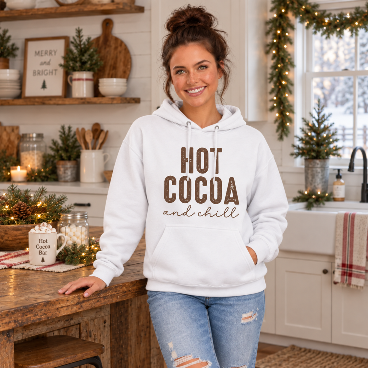 Woman wearing a white hoodie with brown Hot Cocoa and Chill design in a festive winter kitchen