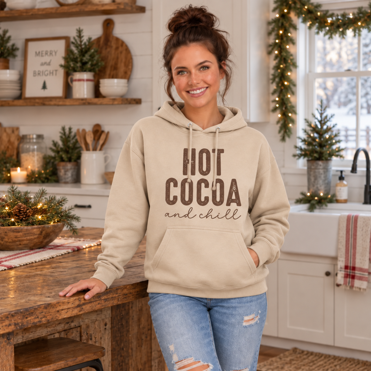 Woman wearing a sand hoodie with brown Hot Cocoa and Chill design in a cozy holiday kitchen