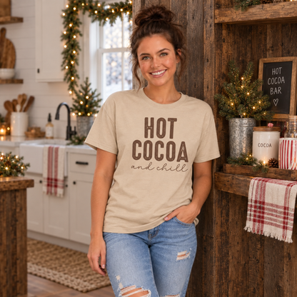 Woman wearing a sand Hot Cocoa and Chill T-shirt beside a rustic hot cocoa bar in a holiday kitchen