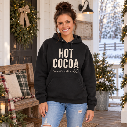 Woman wearing a black hoodie with Hot Cocoa and Chill design on a snowy decorated porch
