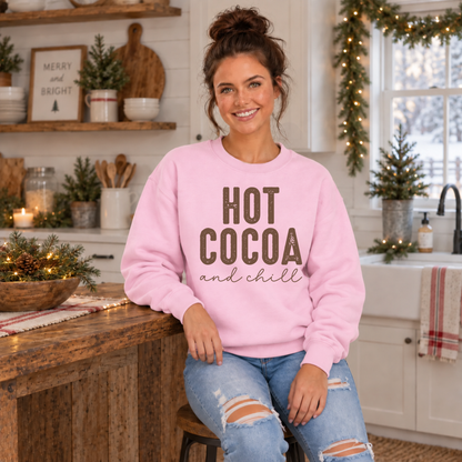 Woman wearing a light pink Hot Cocoa and Chill sweatshirt while seated at a rustic kitchen counter